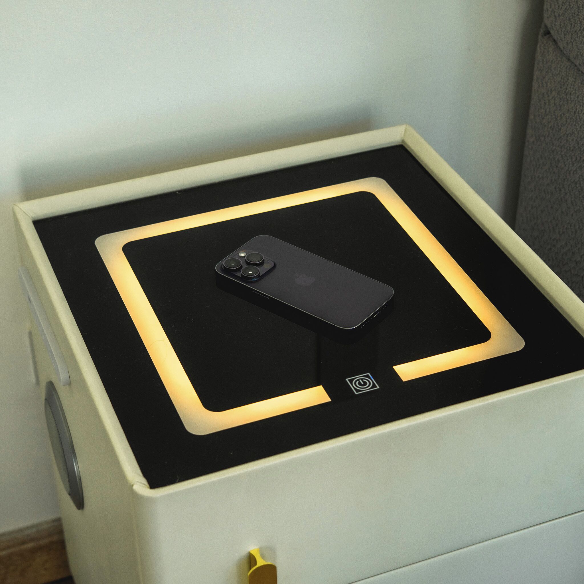 A bedside table with a smartphone on it, a power button, and a drawer.