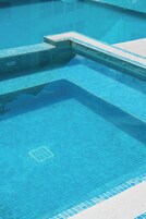 Una piscina con agua azul cristalina, escalones de cerámica y una rejilla de desagüe.