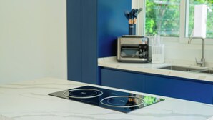 A modern kitchen with a white marble countertop, a black induction cooktop, and a coffee maker on the counter.