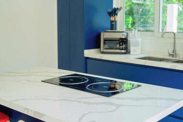 A modern kitchen with a white marble countertop, a black induction cooktop, and a coffee maker on the counter. - T Loft (Playa Hermosa)