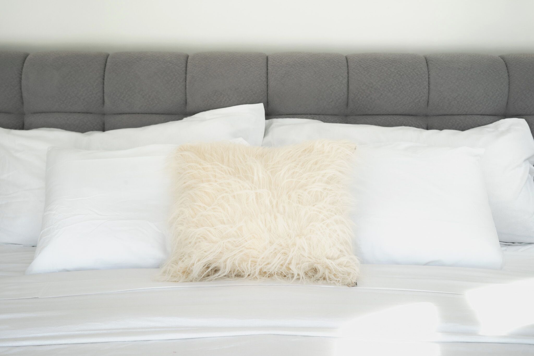 Un lit avec une tête de lit rembourrée de couleur grise, une literie blanche et un oreiller beige moelleux.