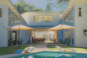 A modern house with a swimming pool, two umbrellas, and a patio area.