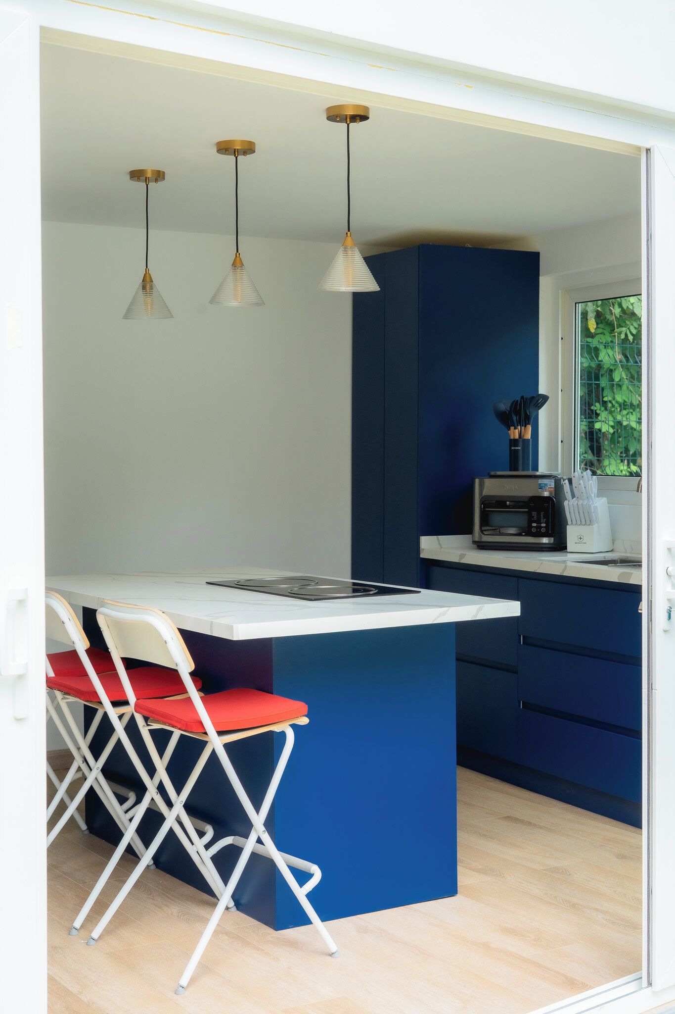 A modern kitchen with a blue island, white bar stools, and pendant lighting.