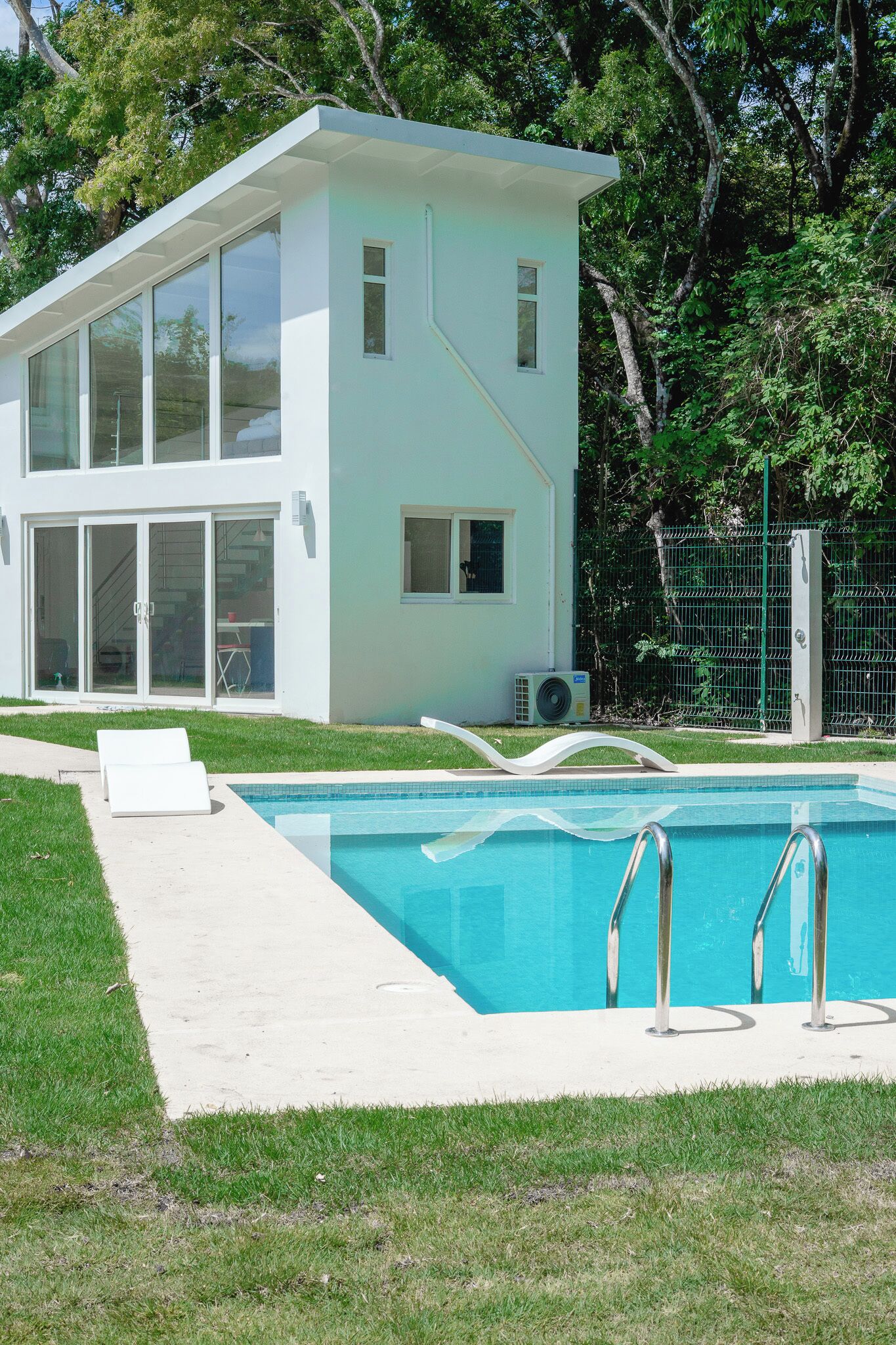 Une maison moderne dotée d’une piscine, de grandes fenêtres et d’une clôture verte.