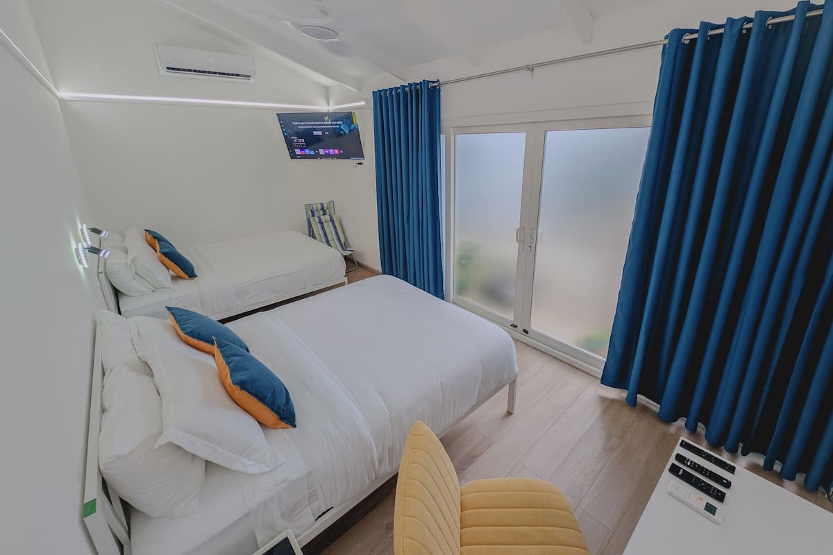 Habitación de hotel con una cama, una silla, un televisor y un ventanal corredera al exterior.