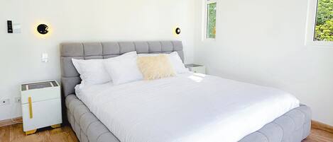 A bedroom with a large bed, a ceiling fan, an air conditioner, a nightstand, and a bedside table.