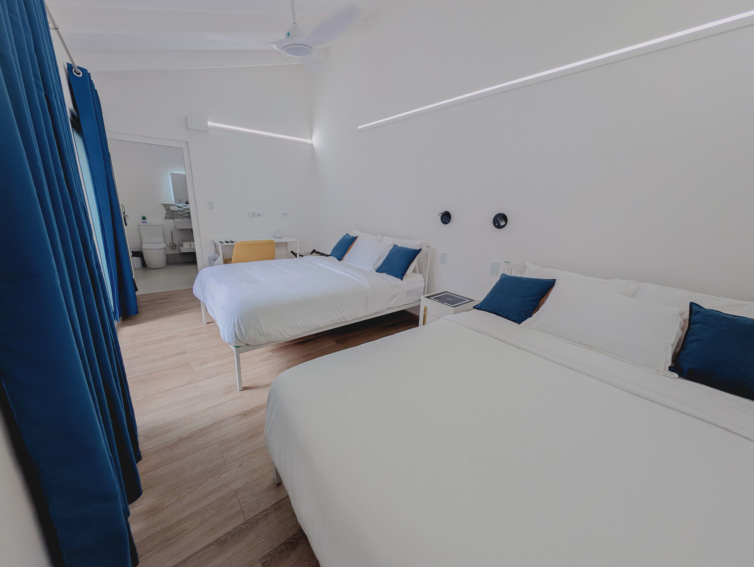 A modern hotel room with two beds, a desk, and a bathroom.