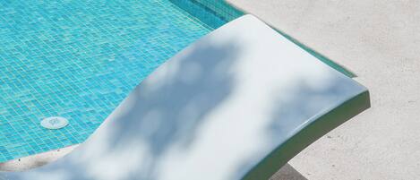Una piscina con tobogán y dos sillas reclinables en una terraza de concreto.
