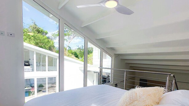 A modern bedroom with a large bed, a ceiling fan, and large windows offering a view of the outdoors. - T Loft (Playa Hermosa)