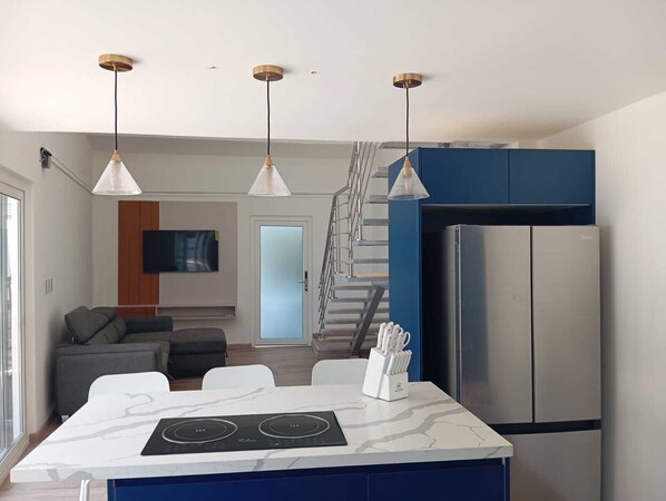 Une cuisine moderne dotée d’un îlot central intégré, d’appareils électroménagers en acier inoxydable, de luminaires suspendus et d’un escalier menant à un espace de vie.