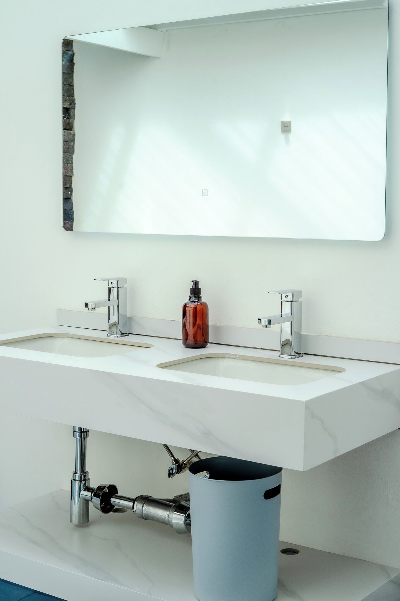 A modern bathroom with two sinks, a large mirror, and a trash can.