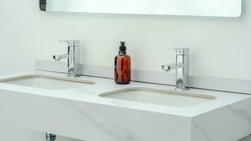A modern bathroom with two sinks, a large mirror, and a trash can.