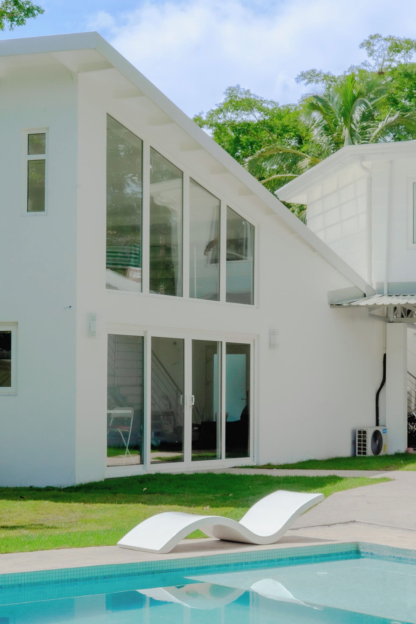 Una casa moderna de dos pisos con ventanas amplias, una piscina y un área de patio techada.