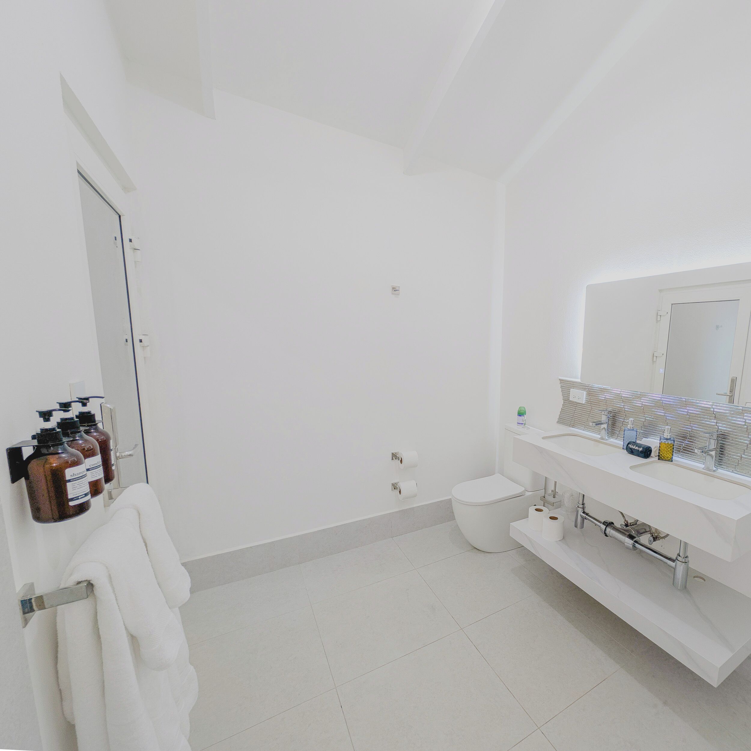 Un bagno moderno con lavandino, specchio e servizi igienici bianchi. Sono presenti articoli da toilette a parete e un porta asciugamani.