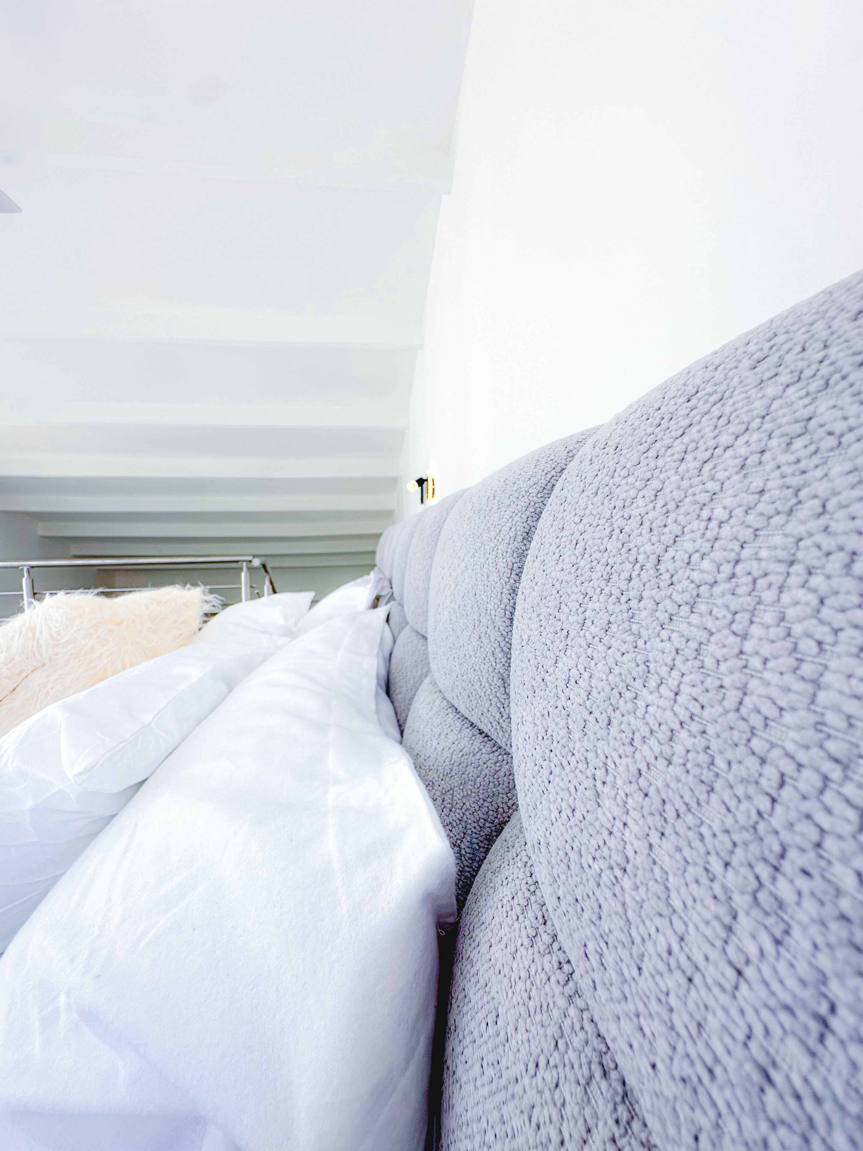 A modern bedroom with a large bed, white bedding, and a grey textured headboard.