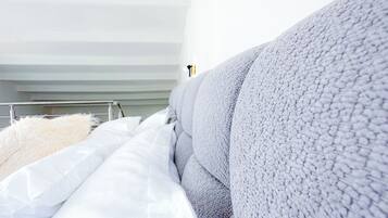A modern bedroom with a large bed, white bedding, and a grey textured headboard.