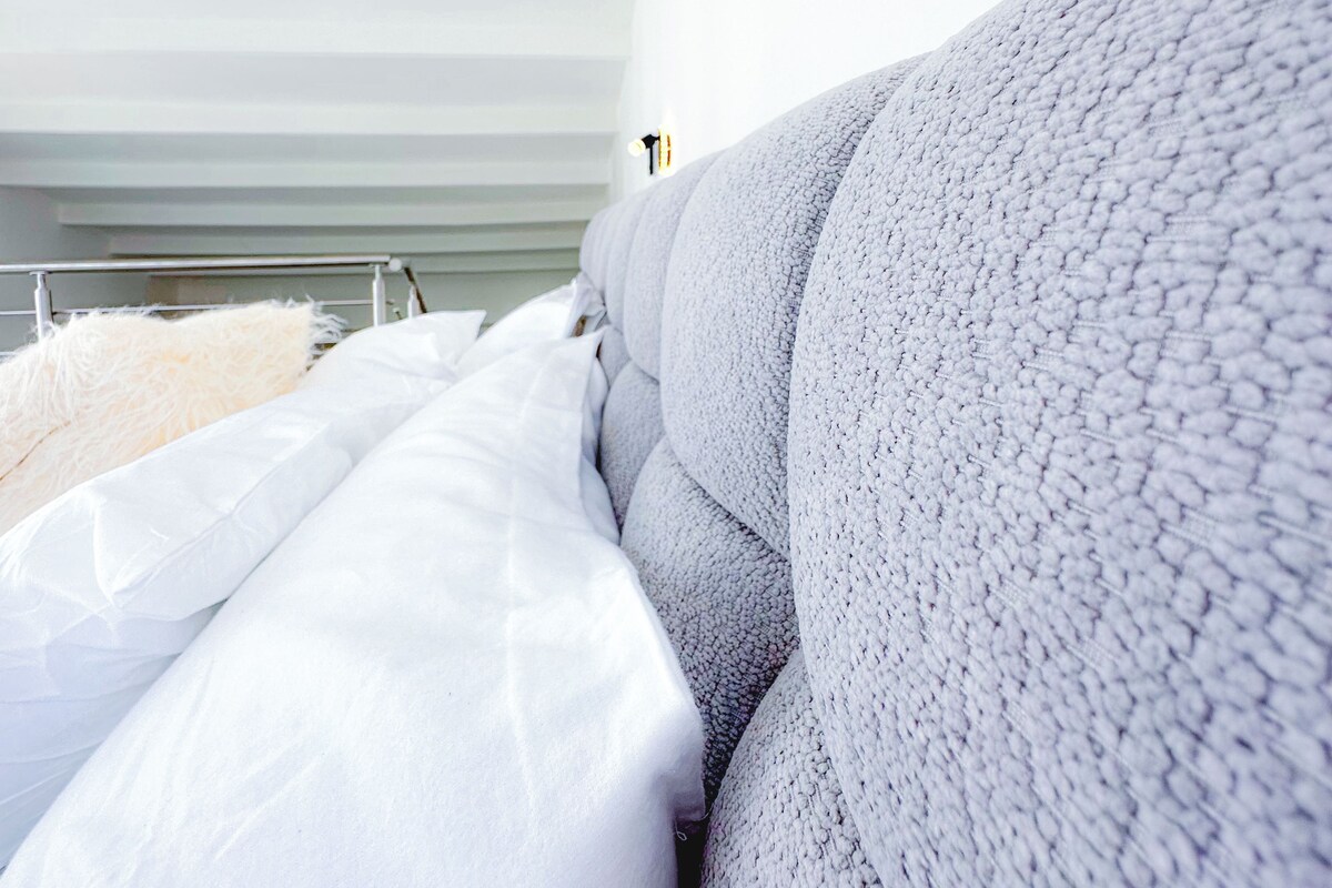 A modern bedroom with a large bed, white bedding, and a grey textured headboard.