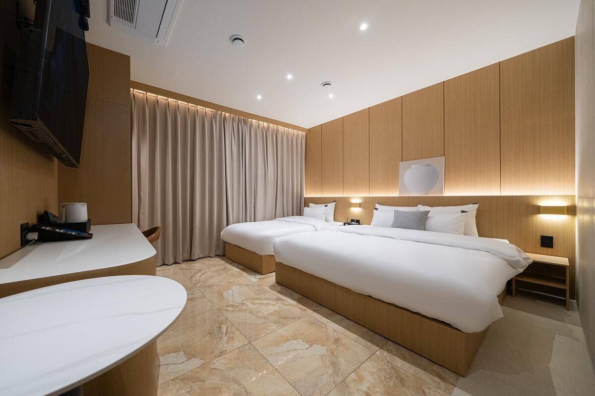 A hotel room with two beds, a desk, a TV, and a large window with curtains.