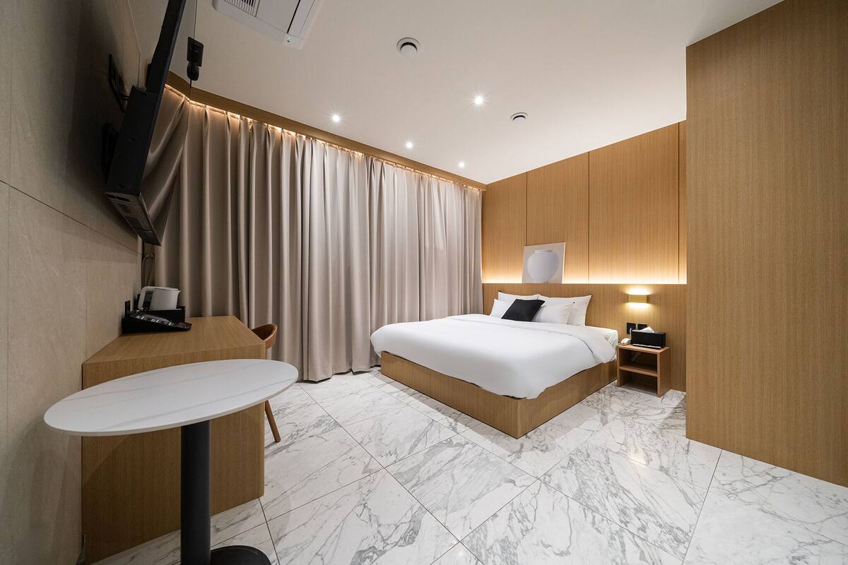A modern hotel room with a large bed, a bedside table, a desk, and a TV mounted on the wall.