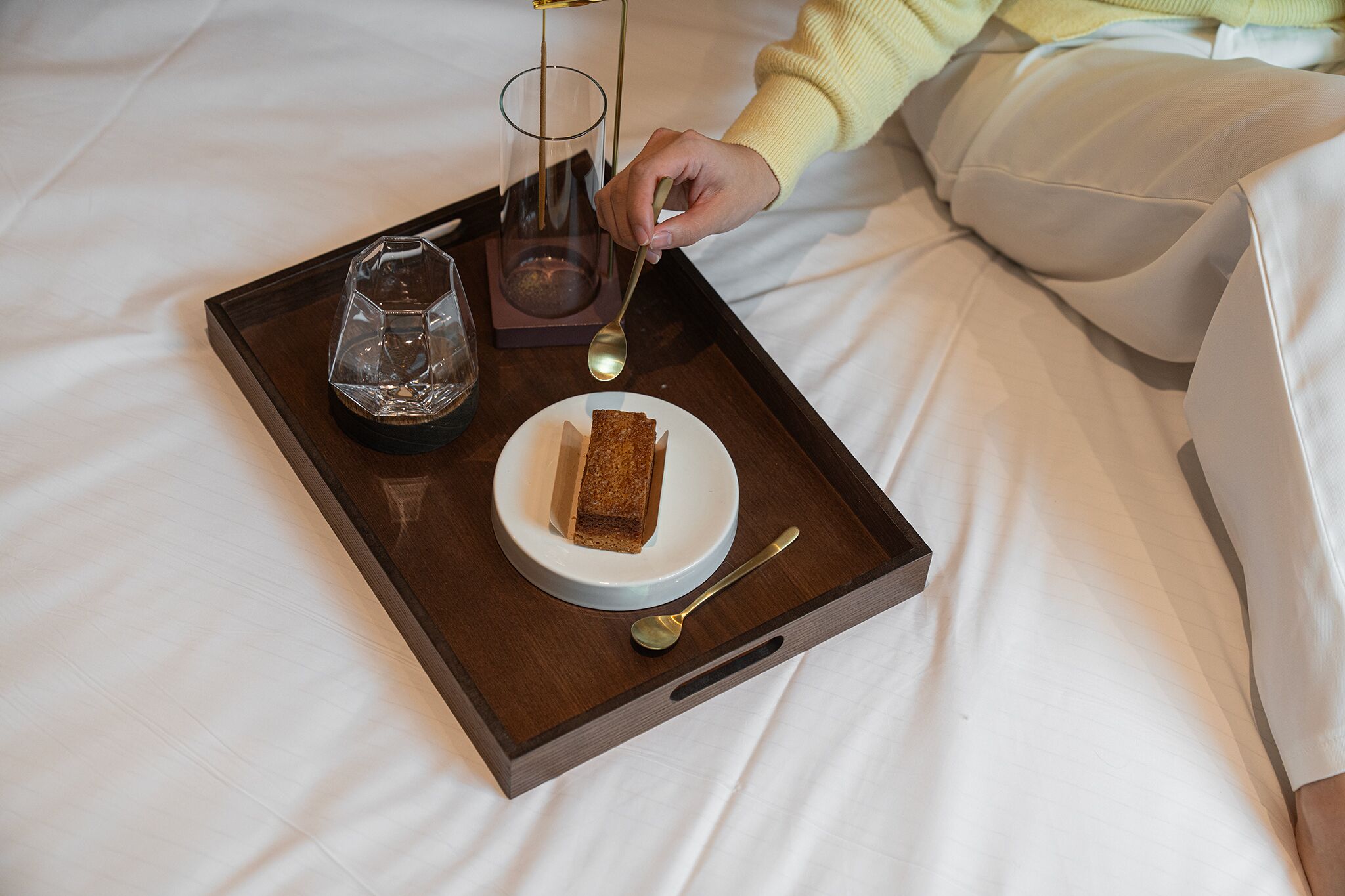 Ein Tablett mit einem Glas, einem Löffel und einem Stück Kuchen auf einem Bett.