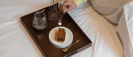 Ein Tablett mit einem Glas, einem Löffel und einem Stück Kuchen auf einem Bett.