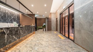 A modern reception area with a marble counter, a green sofa, and a plant. - Incheon Brown-Dot Hotel (Incheon)