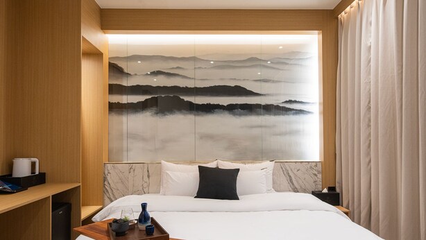 A modern hotel room with a large bed, a wooden nightstand, a marble headboard, and a wall-mounted artwork depicting a mountainous landscape. - Incheon Brown-Dot Hotel (Incheon)