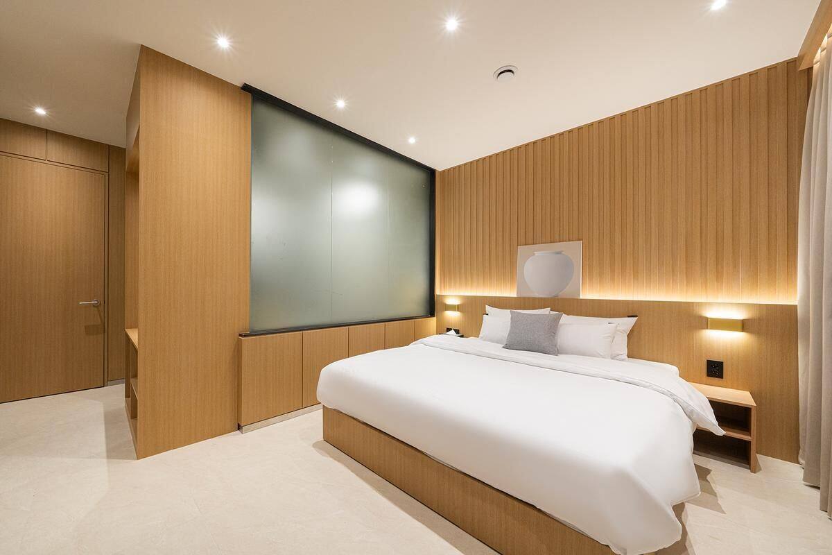 A modern hotel room with a large bed, wooden paneling, a flat-screen TV, and a bedside table with a lamp.
