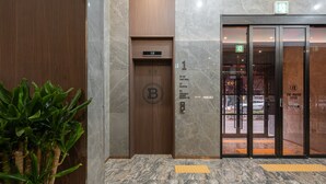 A hotel entrance with a marble floor, a wooden elevator, and a glass door with a sign indicating room numbers. - Incheon Brown-Dot Hotel (Incheon)