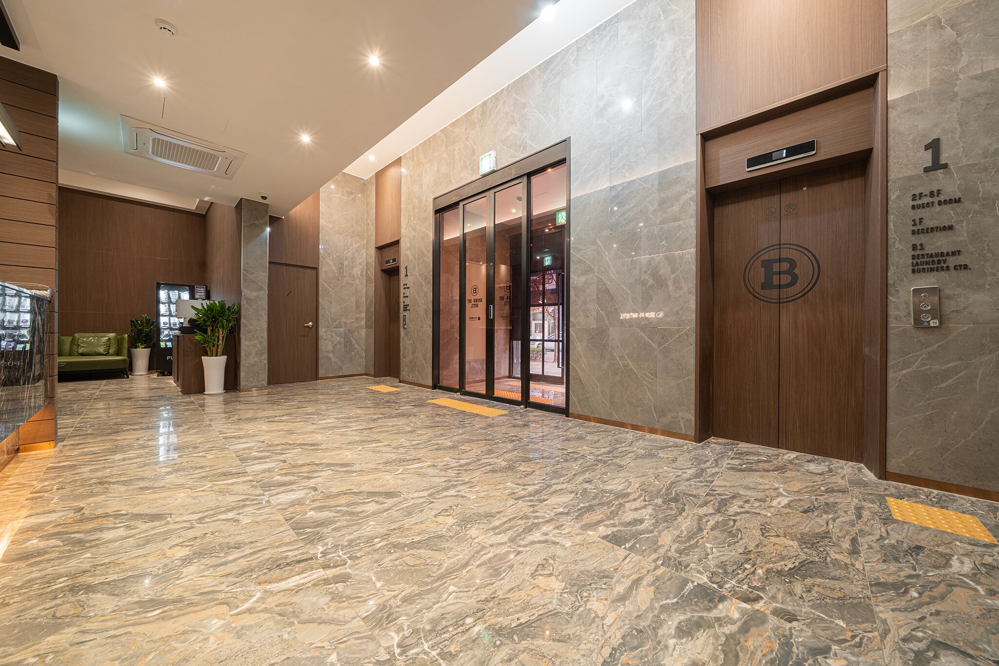 A hotel lobby with a marble floor, wooden paneling, a reception desk, and a guest room sign.