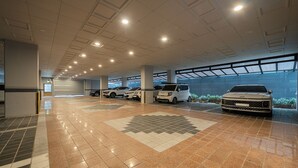 A spacious parking garage with multiple cars parked, a tiled floor, and a ceiling with recessed lighting. - Incheon Brown-Dot Hotel (Incheon)