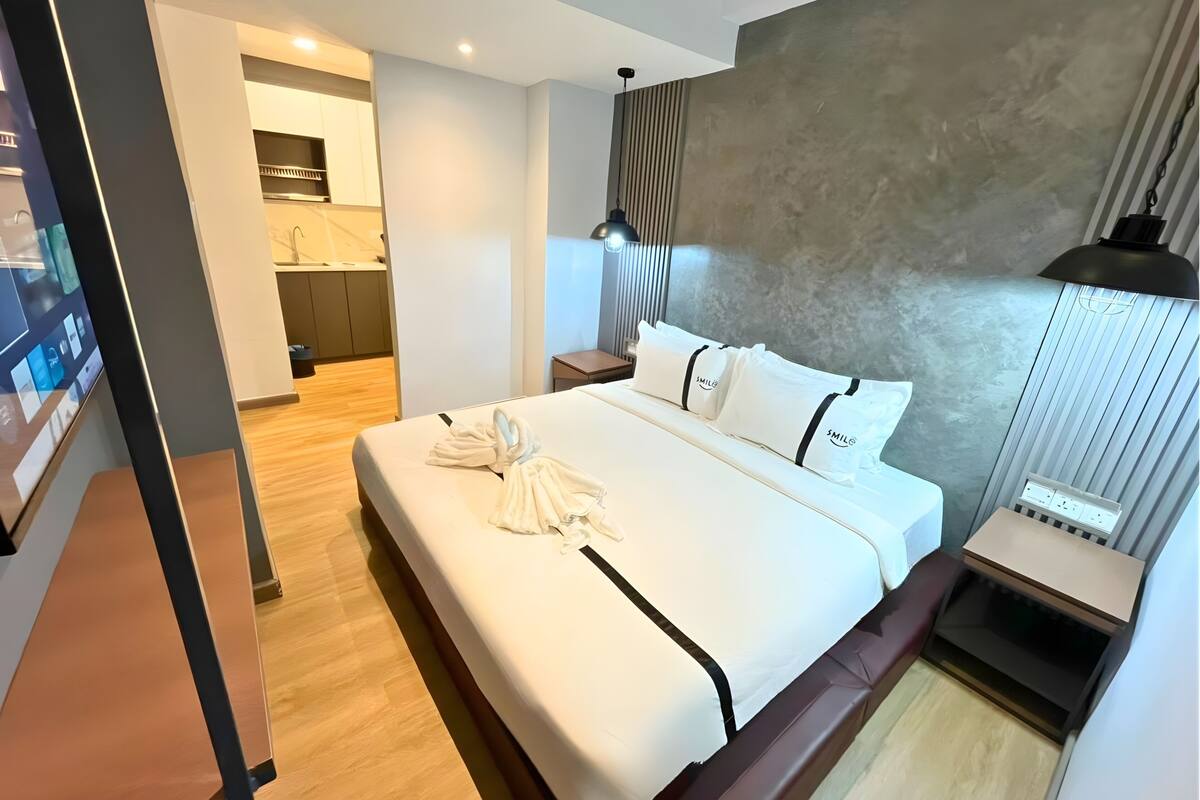 Une chambre d’hôtel moderne dotée d’un grand lit, d’une table de chevet, d’une petite table, d’une lampe fixée au mur et d’un téléviseur intégré.