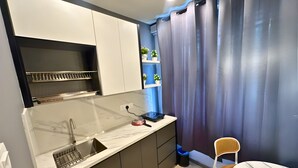 A compact kitchen with a sink, countertop, and a small dining area with a chair and table. - Seeds Hotel Bukit Bintang (Kuala Lumpur)