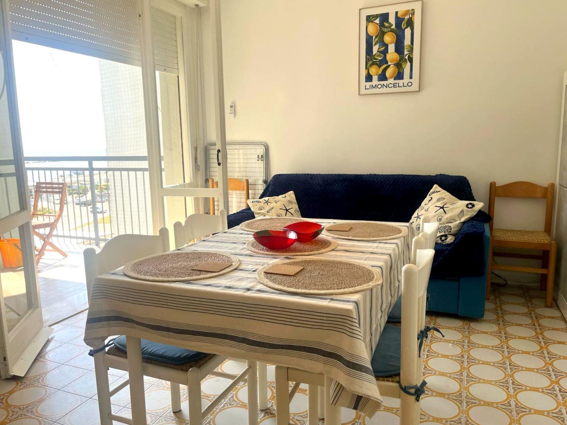 A dining area with a table set for two, a blue sofa, and a chair.