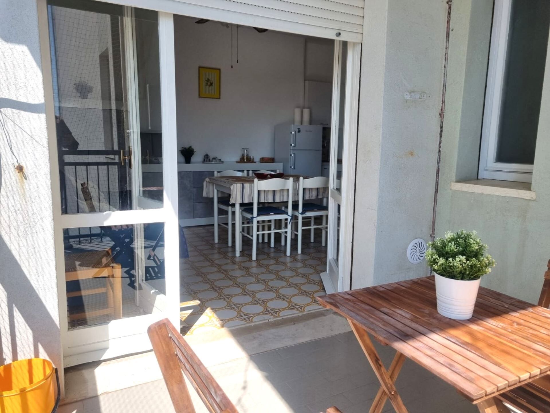 A patio area with a wooden table and chairs, a potted plant, and a view into a kitchen with a dining table and chairs.