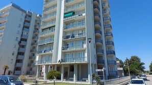 A multi-story residential building with balconies, a covered entrance, and a clear sky. - Cortina 2-24 Comfortable two-room apartment facing the sea (Comacchio)