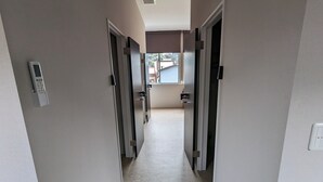 A hallway with doors leading to rooms, a thermostat on the wall, and a window at the end. - ATARAYO - Hostel (Shimoda)