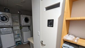 A laundry room with stacked laundry, a washing machine, a dryer, and a sign indicating the shower room is for women only. - ATARAYO - Hostel (Shimoda)