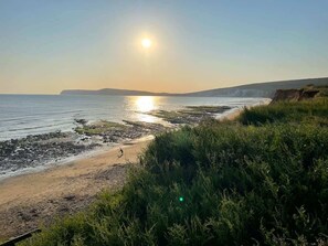 A coastal landscape with a beach, vegetation, and a clear sky. - Charming 2-Bed Family Cottage Your West Bay Retrea (Yarmouth)