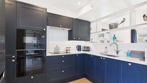 A modern kitchen with dark blue cabinets, a built-in oven, a microwave, and a sink.