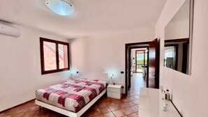 A bedroom with a bed, bedside table, and a mirror. There is a window with curtains and a door leading to another room. - Villetta Volterraio in Rio Elba (Rio dell'Elba)