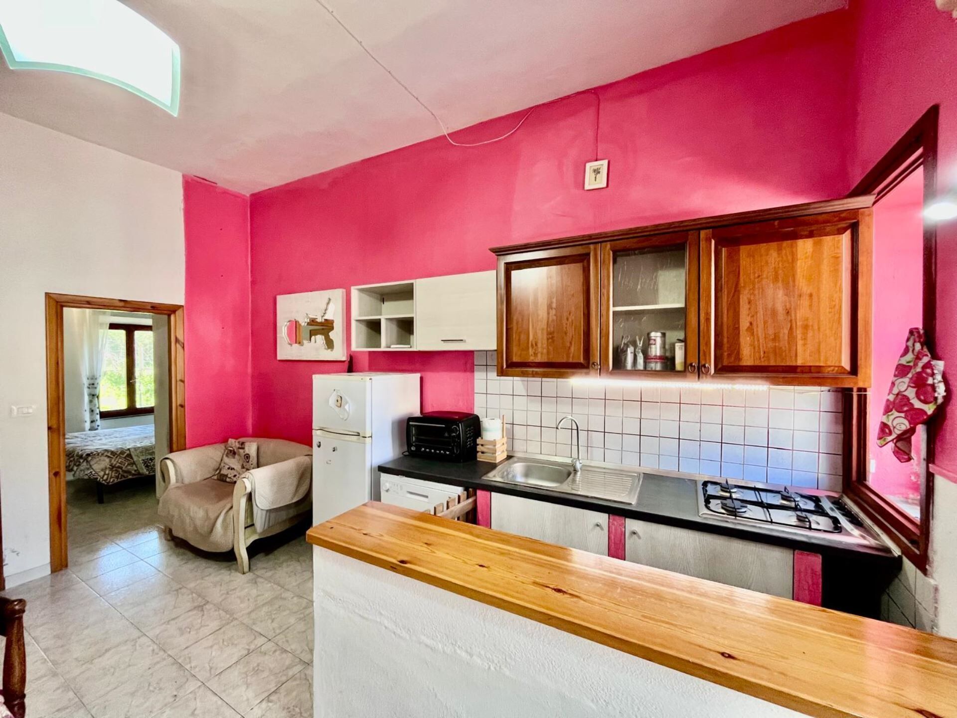 Una cocina compacta con pared rosa, muebles blancos y encimera de madera.