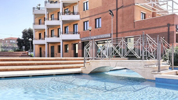 A swimming pool with a bridge leading to a building labeled "Cassa di Risparmio di Volterra". - TWO-ROOM APARTMENT SLEEPS 5 IN THE CENTRAL AREA (San Vincenzo)