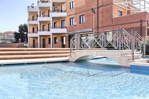 Ein Schwimmbecken mit einer Brücke zu einem Gebäude, auf dem "Cassa di Risparmio di Volterra" steht.