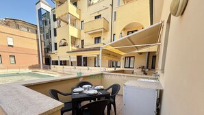 A small outdoor dining area with a table and chairs, a pool in the background, and a building with balconies. - TWO-ROOM APARTMENT SLEEPS 5 IN THE CENTRAL AREA (San Vincenzo)