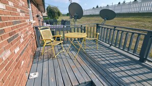 A wooden deck with a brick wall, two satellite dishes, and yellow chairs.