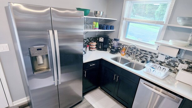 A modern kitchen with a stainless steel refrigerator, black cabinets, a dishwasher, and a window with blinds.