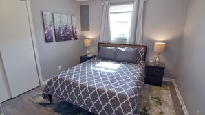 A bedroom with a patterned bedspread, two bedside lamps, a window with curtains, and a door.