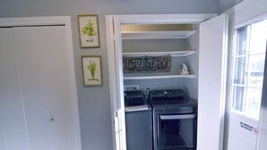 A laundry room with a washer and dryer, a shelf with a 'Laundry' sign, and two framed botanical prints on the wall.