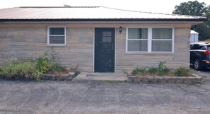 Un edificio de una sola planta con fachada de piedra color beige, una puerta principal negra y dos ventanas con marcos blancos.